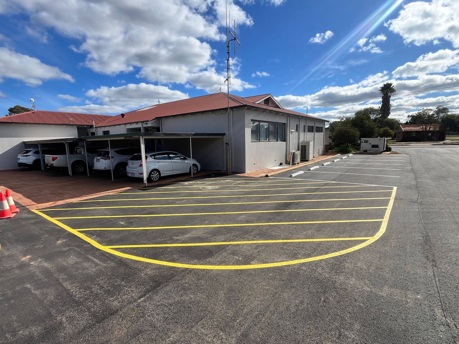 Exterior view of a building with a covered parking area and a curved yellow painted area on the asphalt.