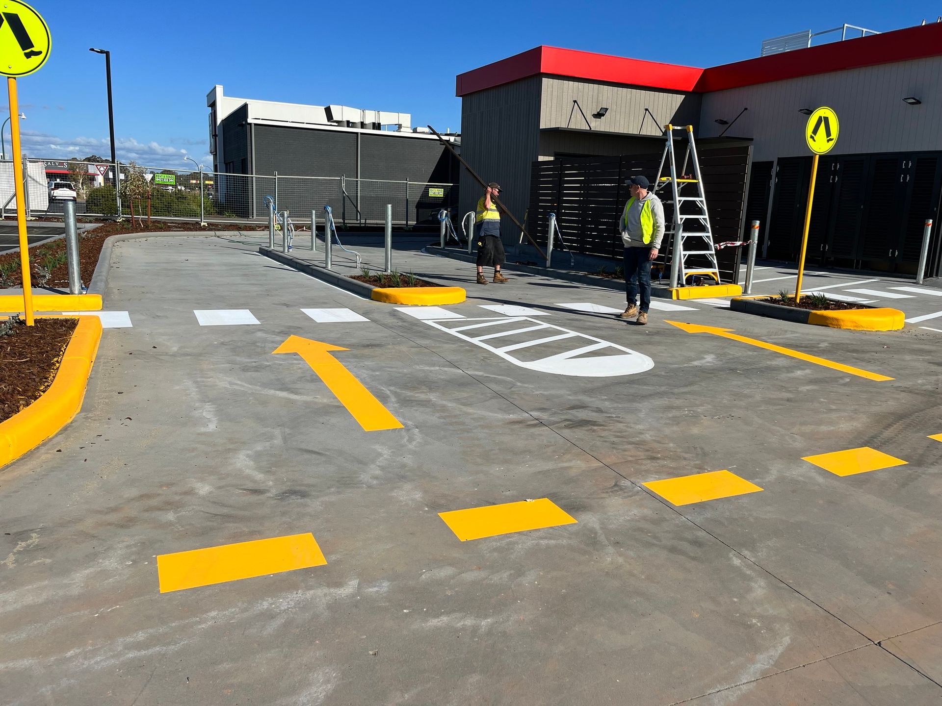 Drive-thru lane with painted arrows and crosswalk. Two people stand near a McDonald's building.