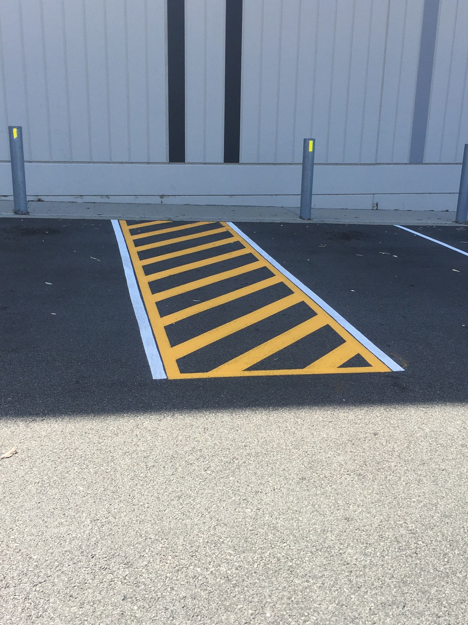 Yellow striped ramp for accessibility, asphalt surface, with metallic posts and gray building in background.