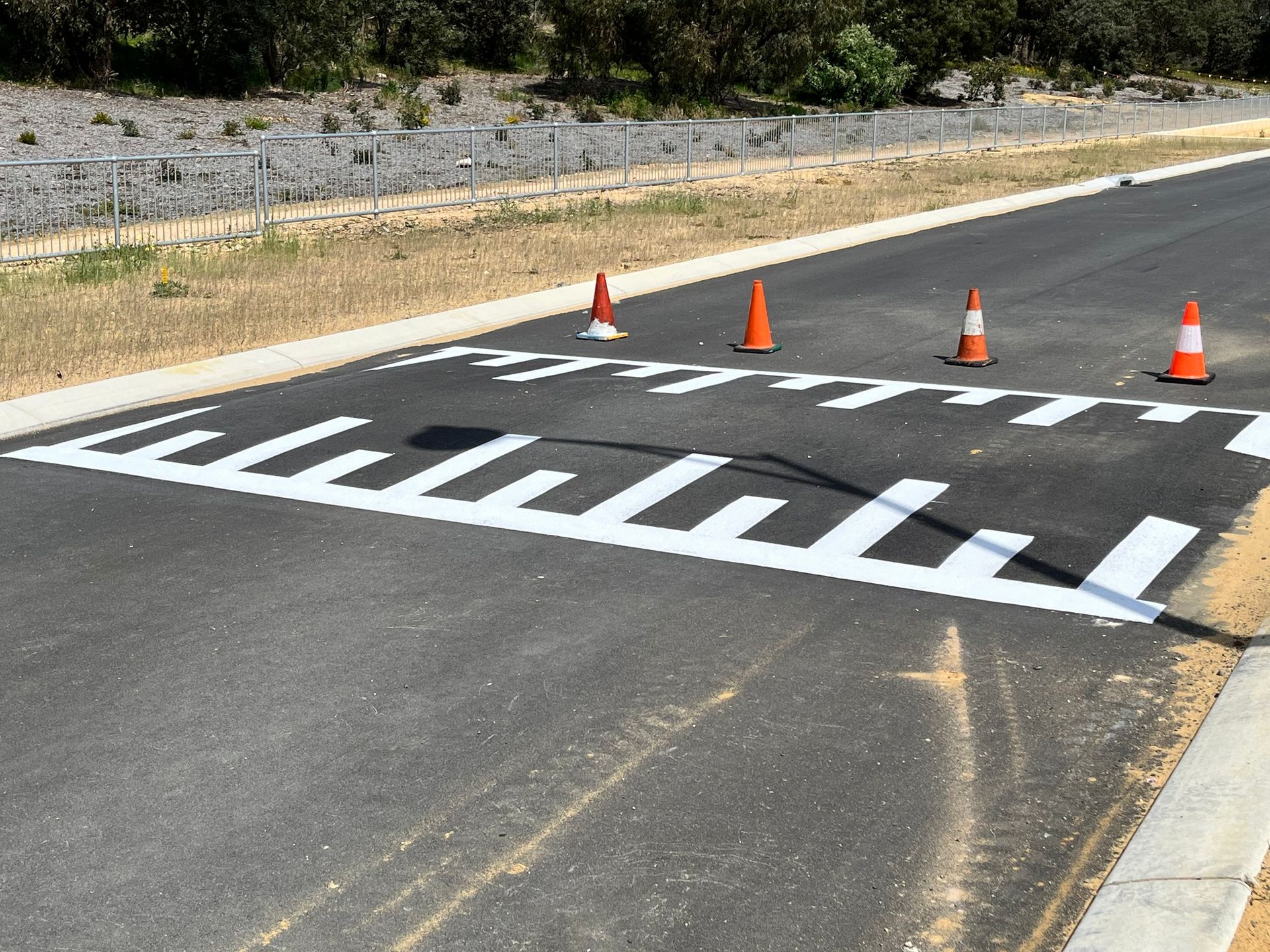 White pavement markings for speed reduction, with orange cones, on an asphalt road.