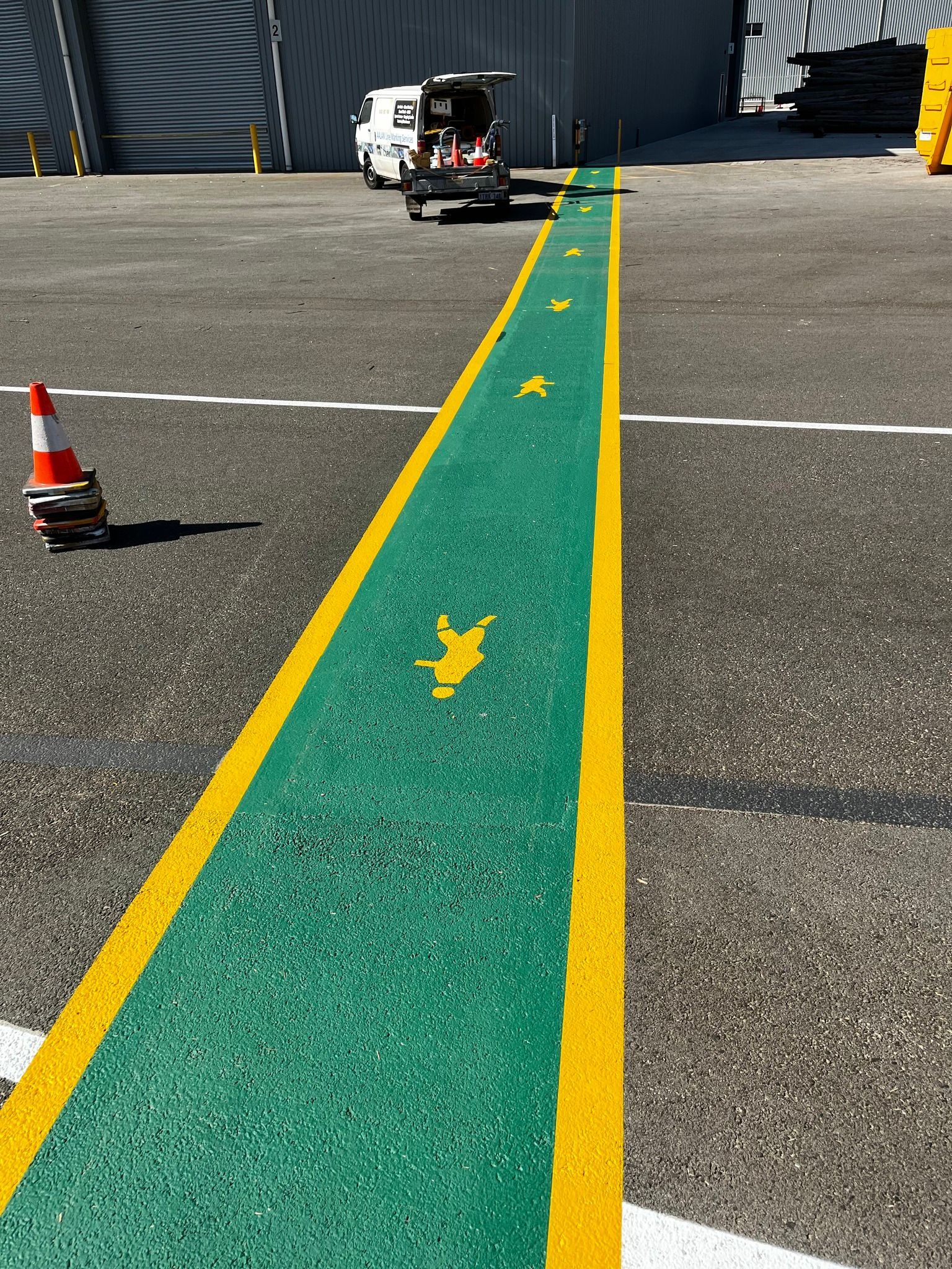 Green and yellow painted path with arrow symbols, leading toward a building. A small vehicle is at the end.