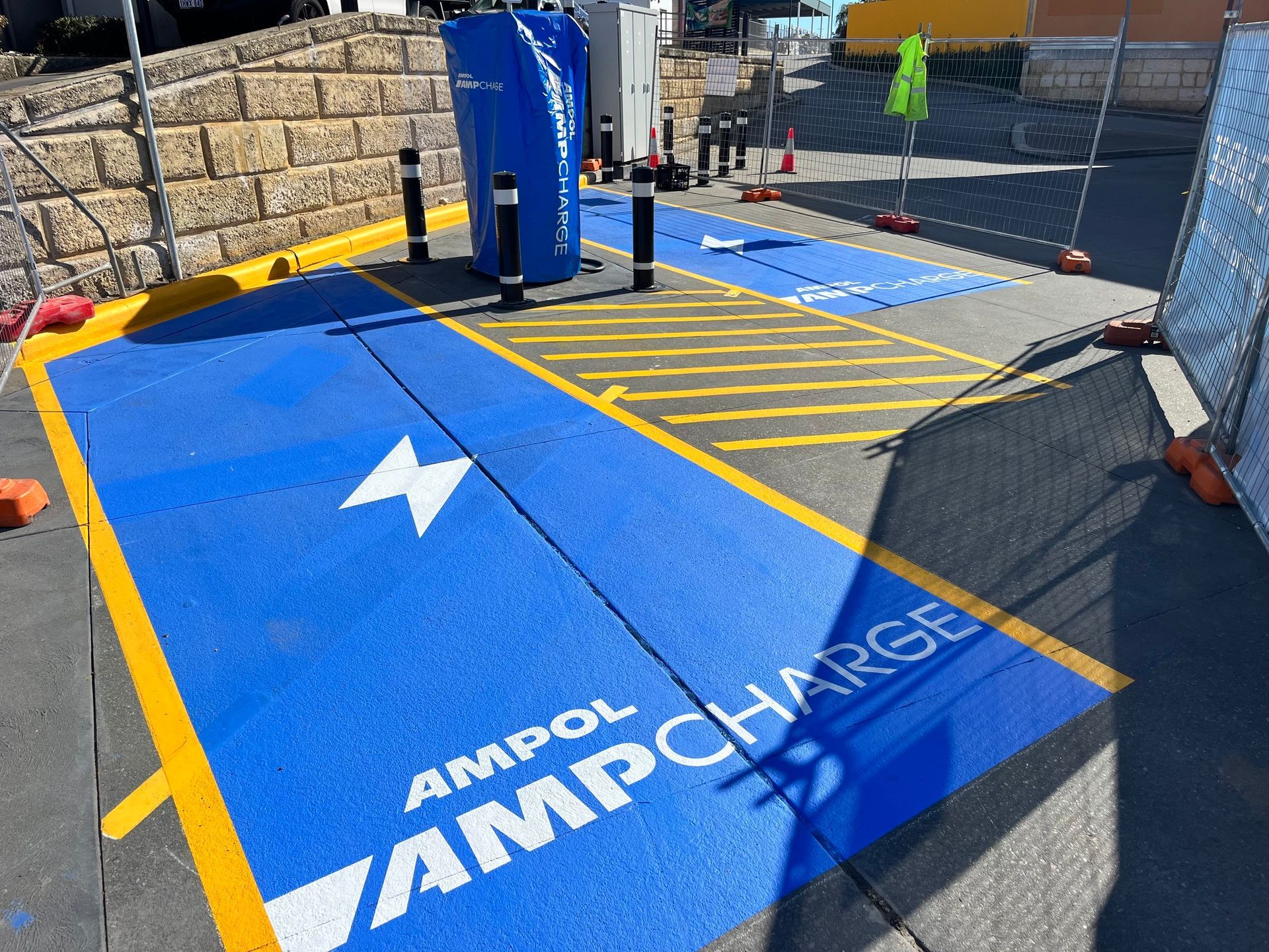 Electric vehicle charging station painted blue with white Ampol logo, charging bays, and yellow markings.