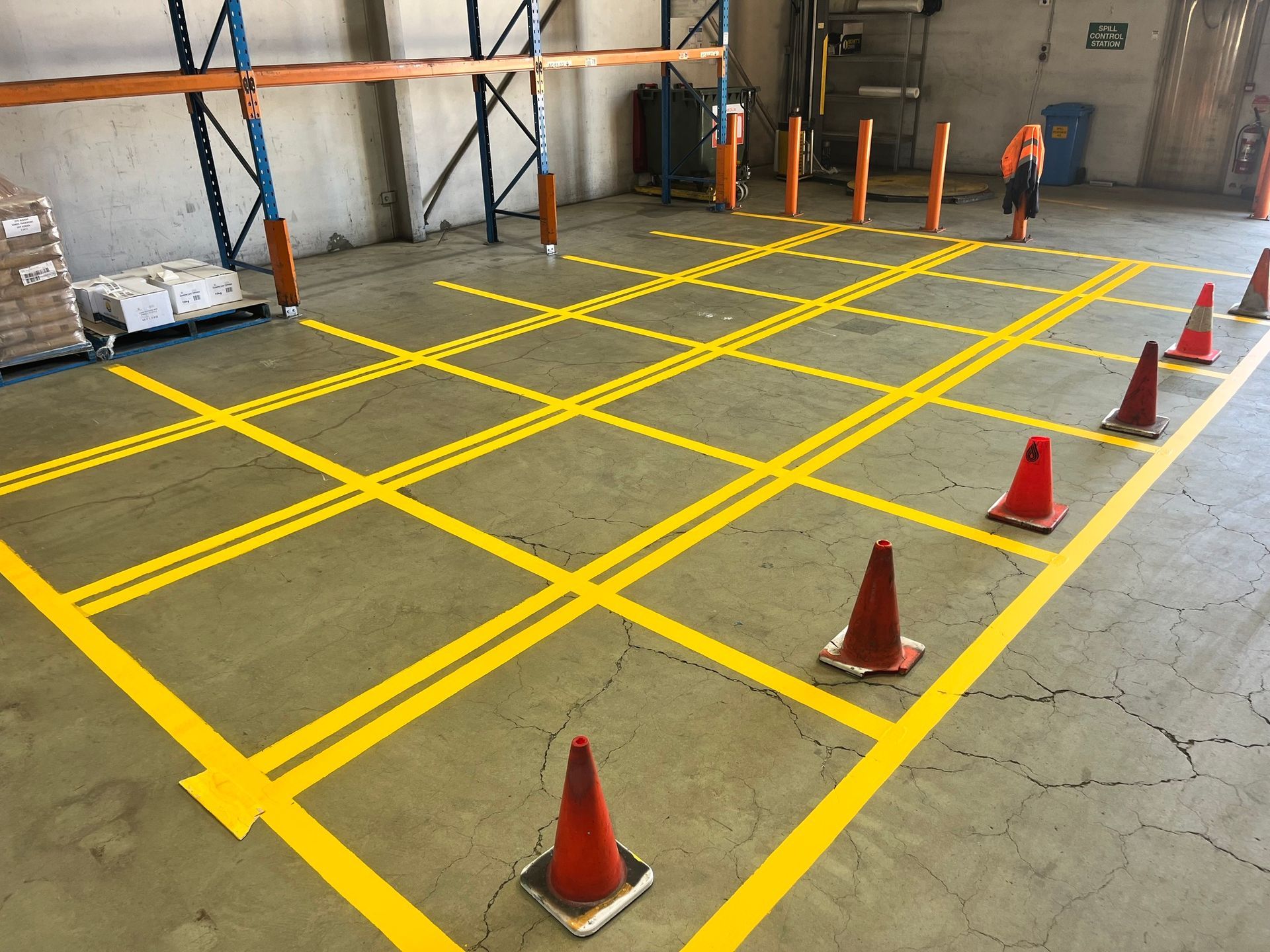 Warehouse floor marked with yellow lines forming squares, orange cones, and a person in the background.