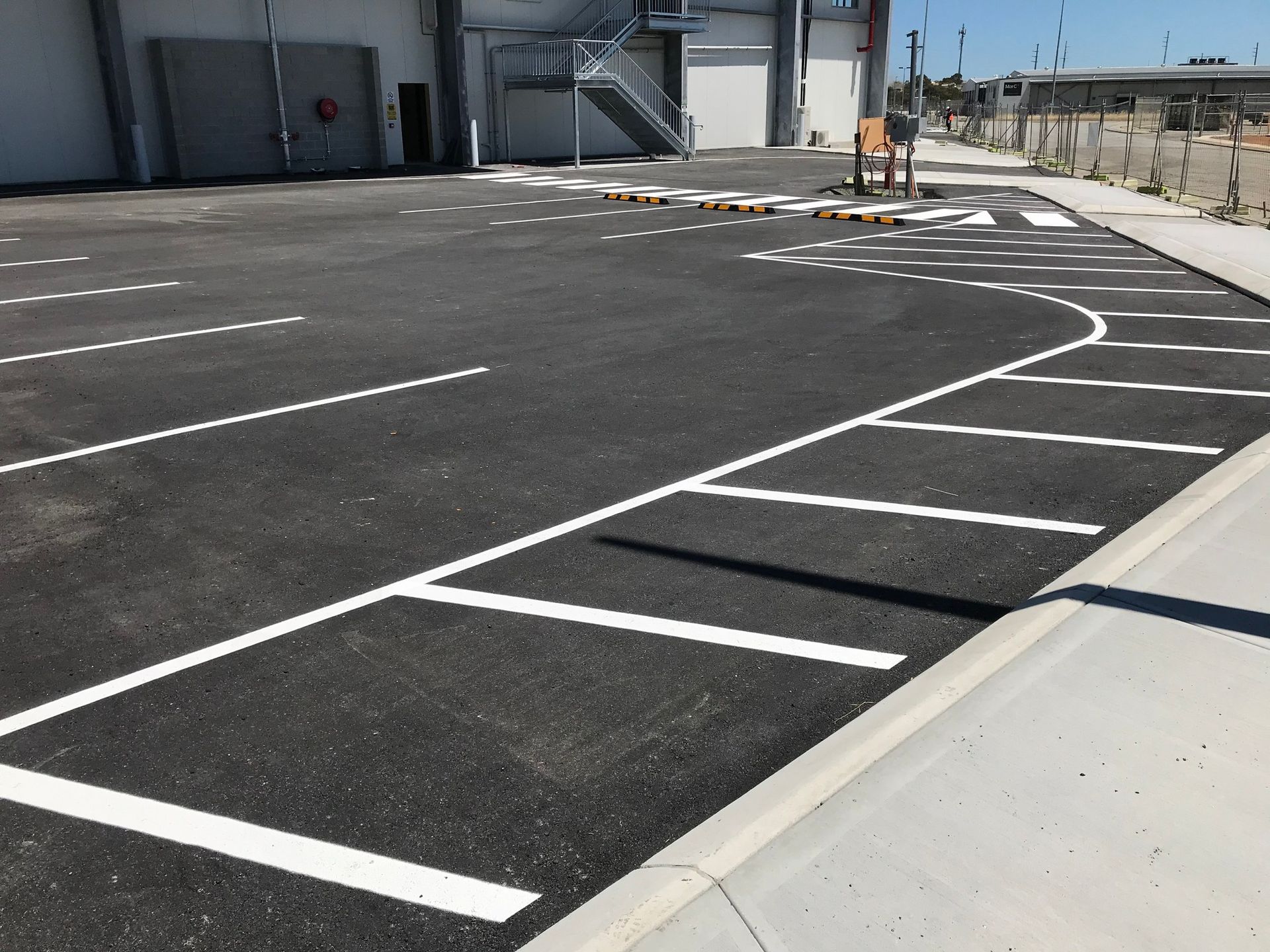 Asphalt parking lot with white painted parking space lines. Concrete curb on the right.