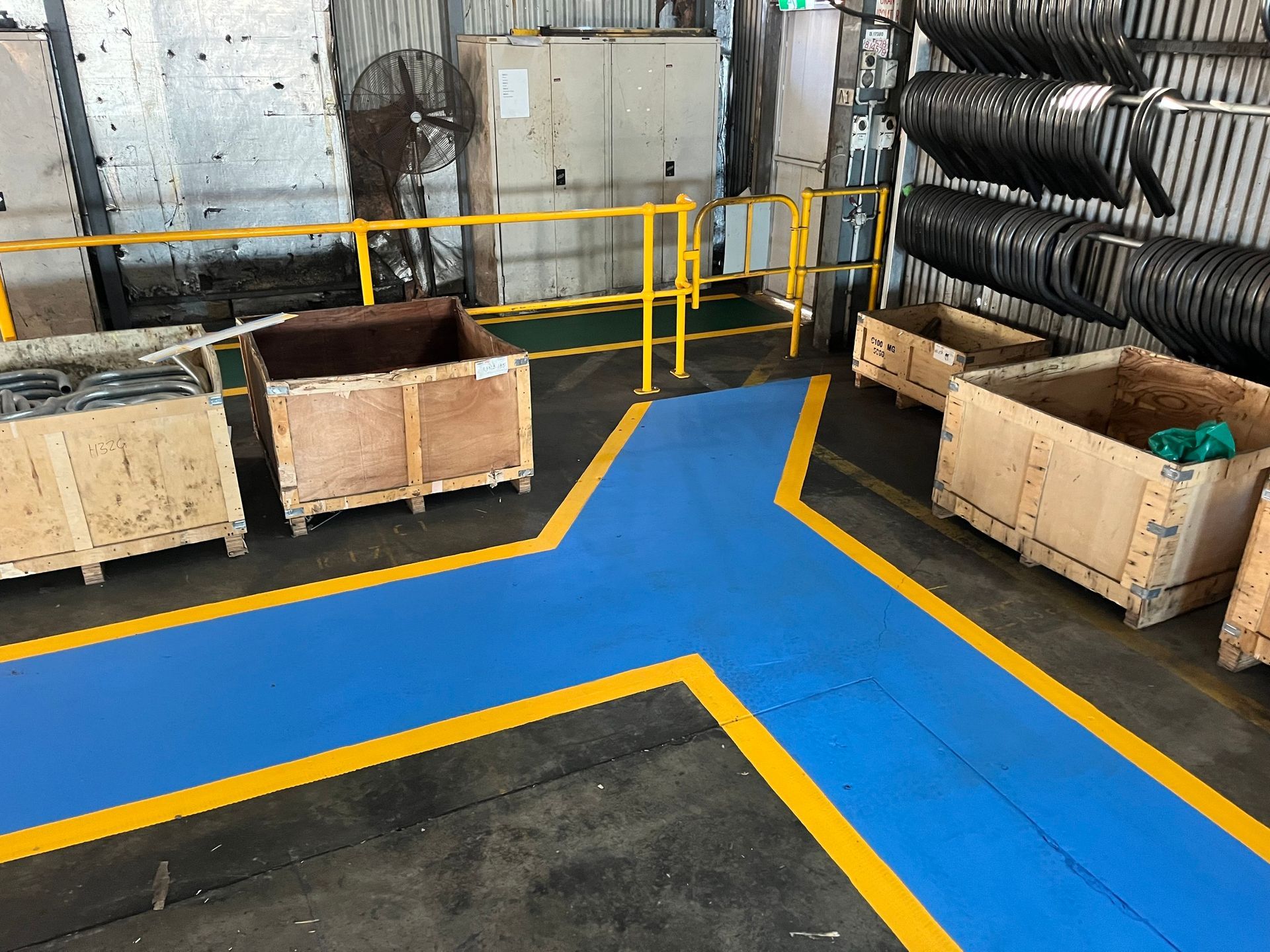Blue and yellow painted pathways in a factory with wooden crates on either side.