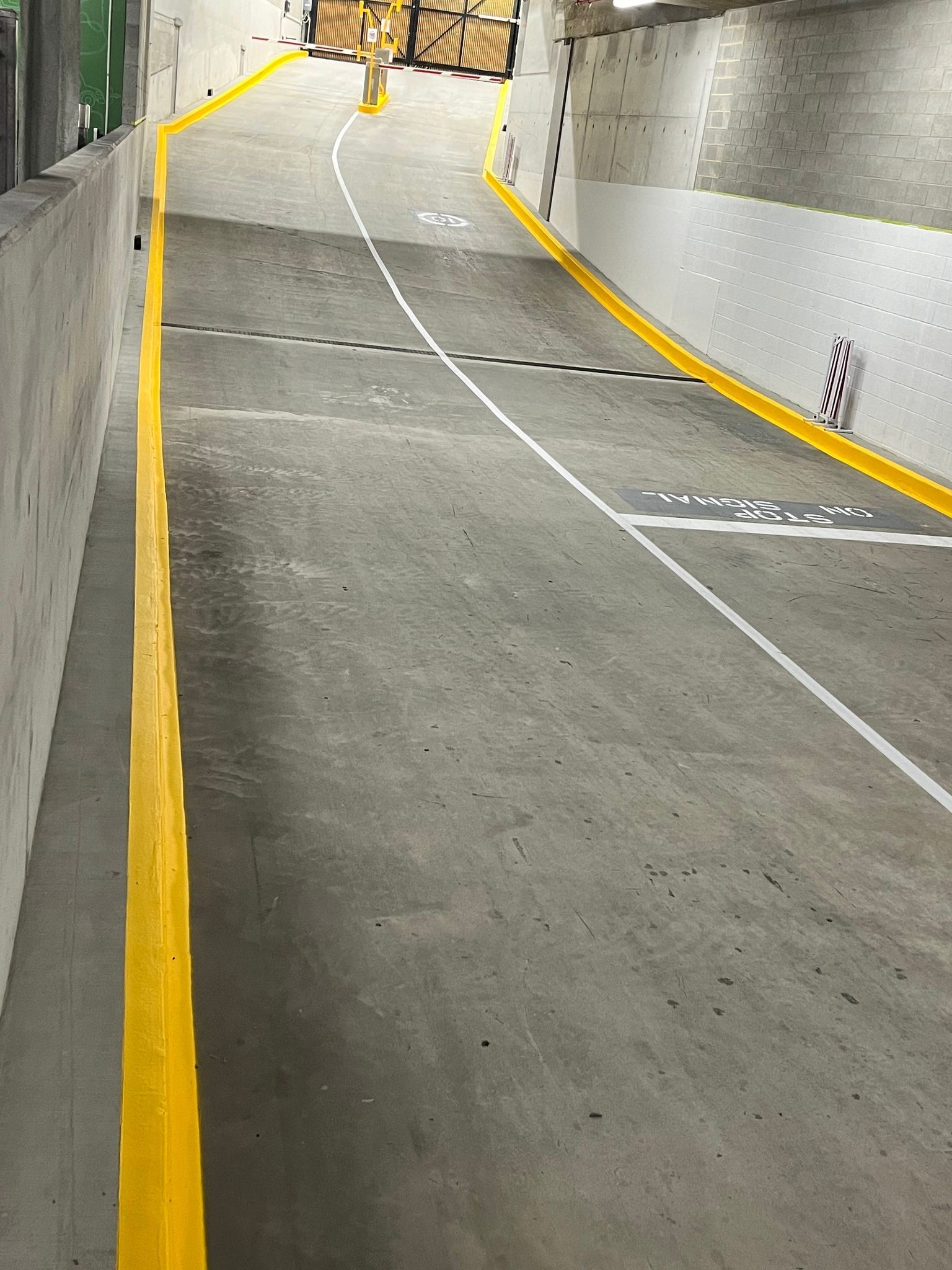 Concrete parking garage ramp with yellow edge markings and white lines.