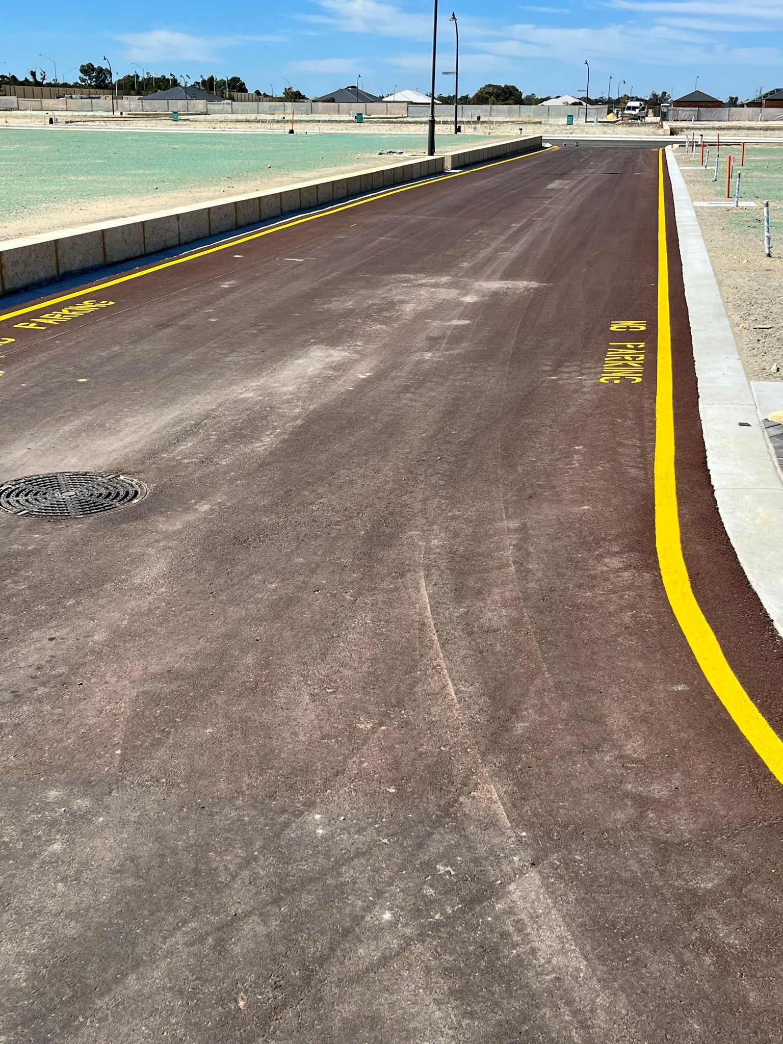 Newly paved road with yellow edge markings, empty lots in the background.