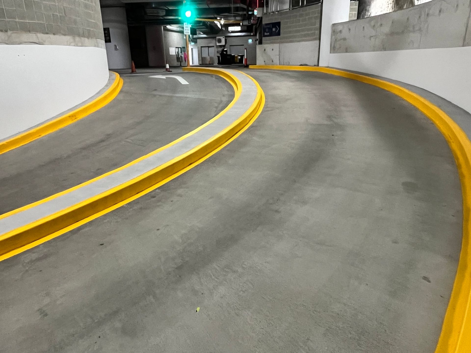 Curved parking garage ramp, concrete surface, yellow curb bumpers, green light ahead.
