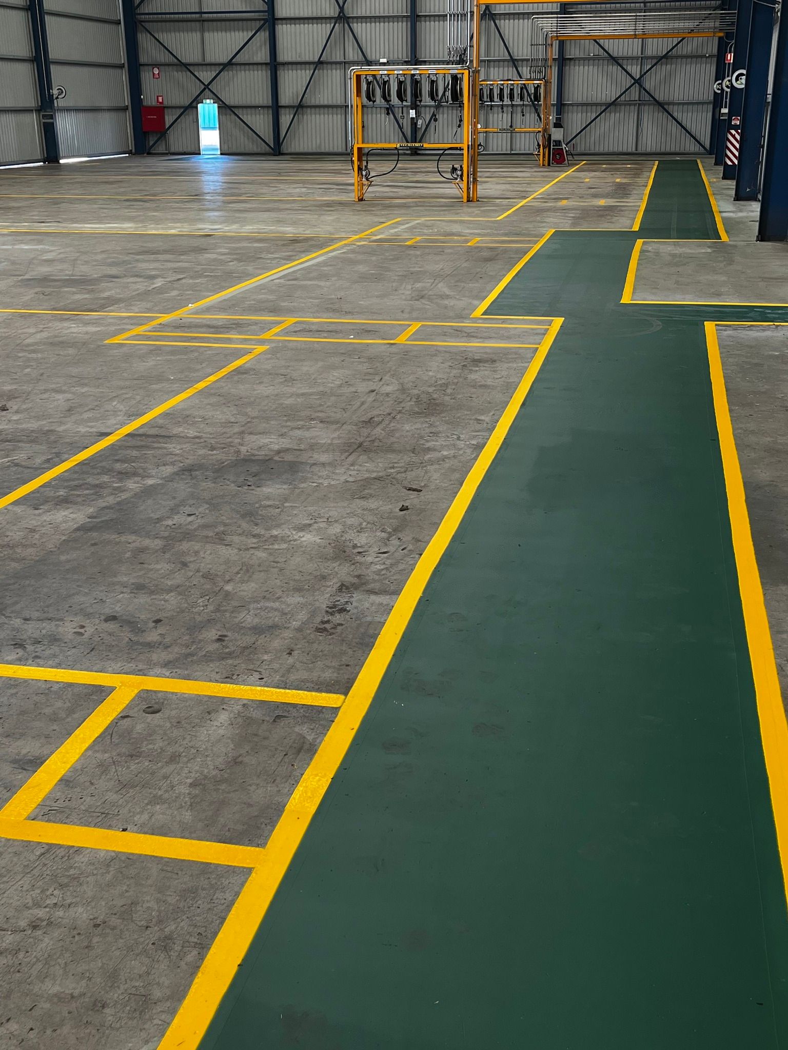 Concrete floor marked with yellow lines and a green lane in a large industrial building.