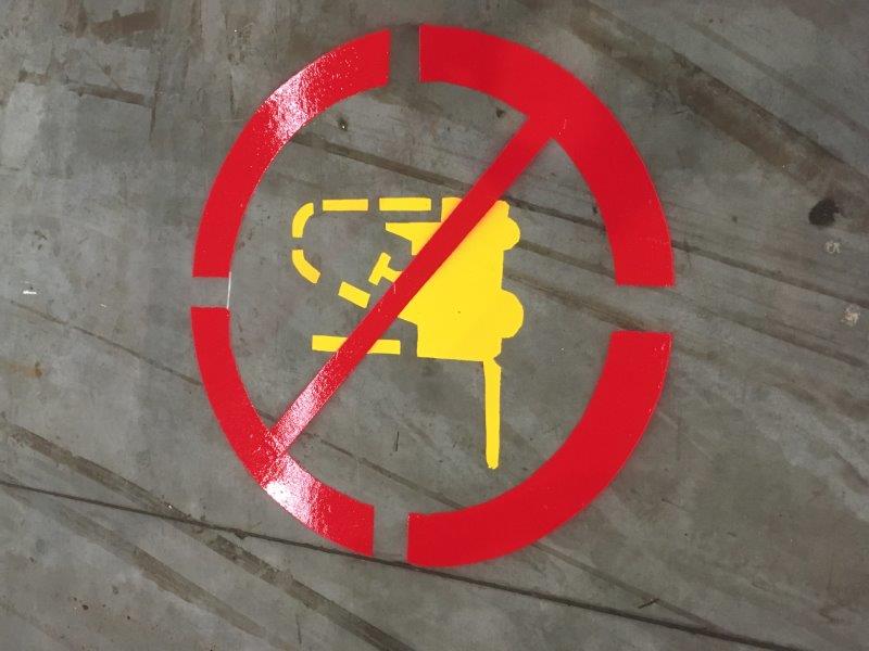 Red circle with a line through a yellow jackhammer; prohibition sign on concrete.