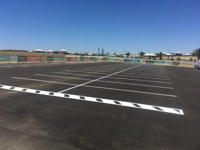 Empty parking lot with white painted lines and a patterned curb on a sunny day.