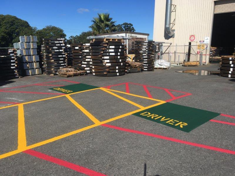 Outdoor area with stacked pallets. Marked parking spots for drivers, painted yellow and red lines.