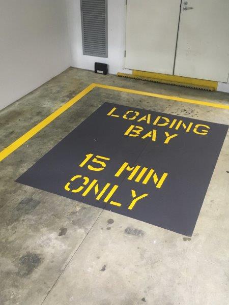 Black and yellow loading bay sign on concrete floor, with a 15-minute time limit.
