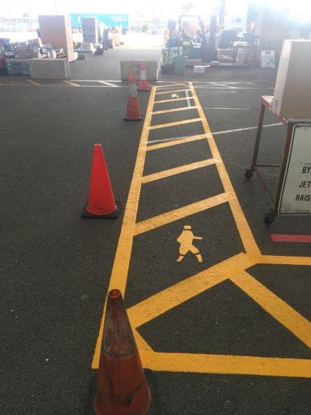 Yellow painted crosswalk with person symbol and orange safety cones on asphalt.
