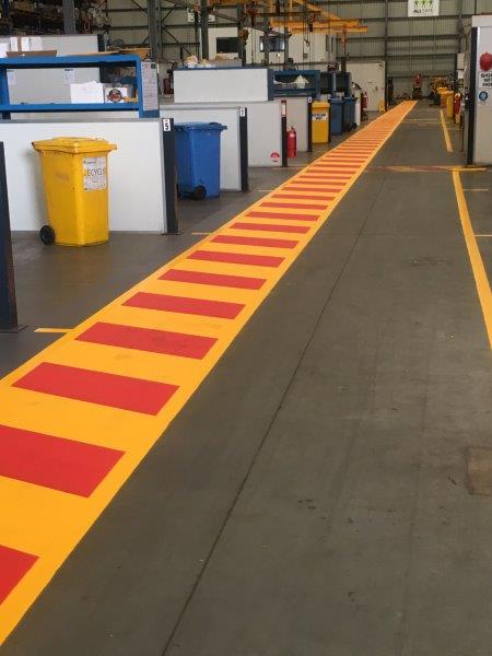 Yellow and red painted pathway markings in an industrial setting.