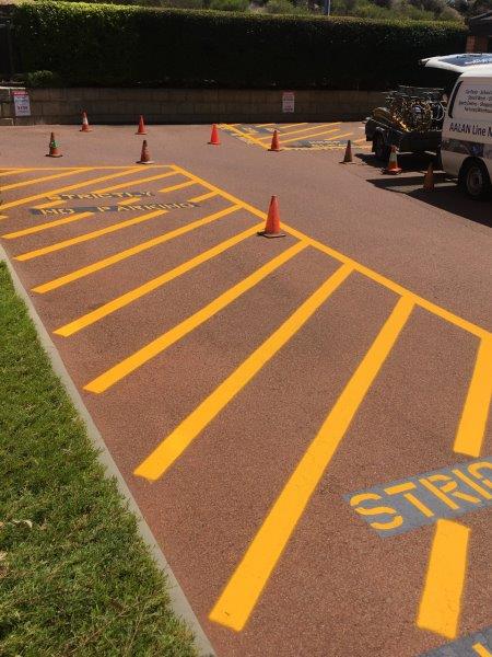 Yellow striped parking spaces on reddish asphalt, orange cones, and parked van.