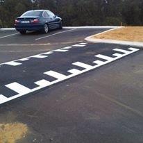 Car in parking spot near a large, white-striped speed bump.