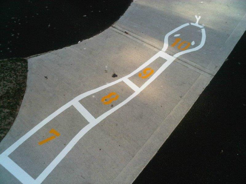 Painted snake-shaped hopscotch on asphalt with numbered squares.