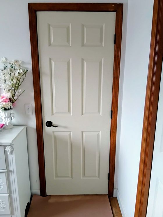 A white door with a wooden frame is in a hallway.