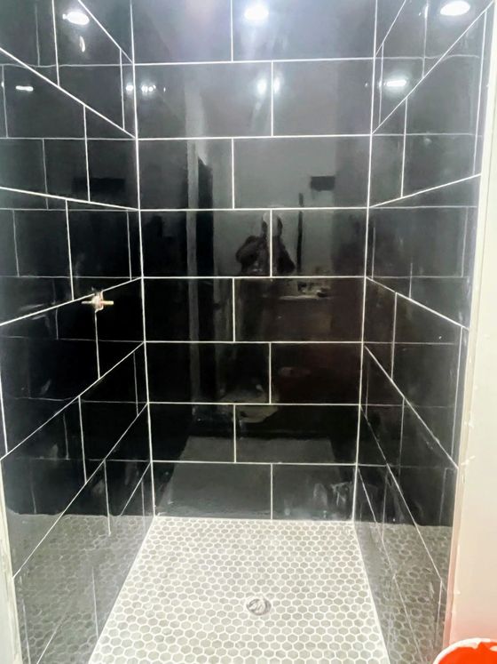 A bathroom with black tiles and a walk in shower.