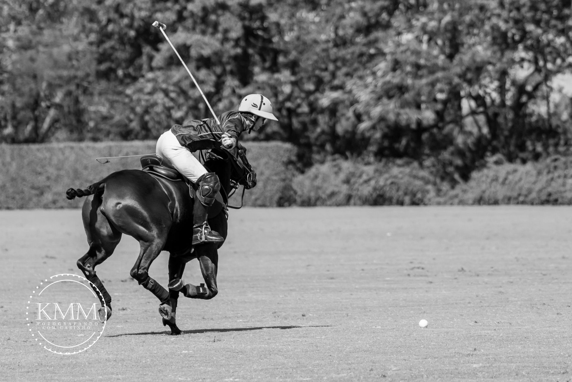 A polo player on a brown horse swings a mallet during a match on a grassy field.
