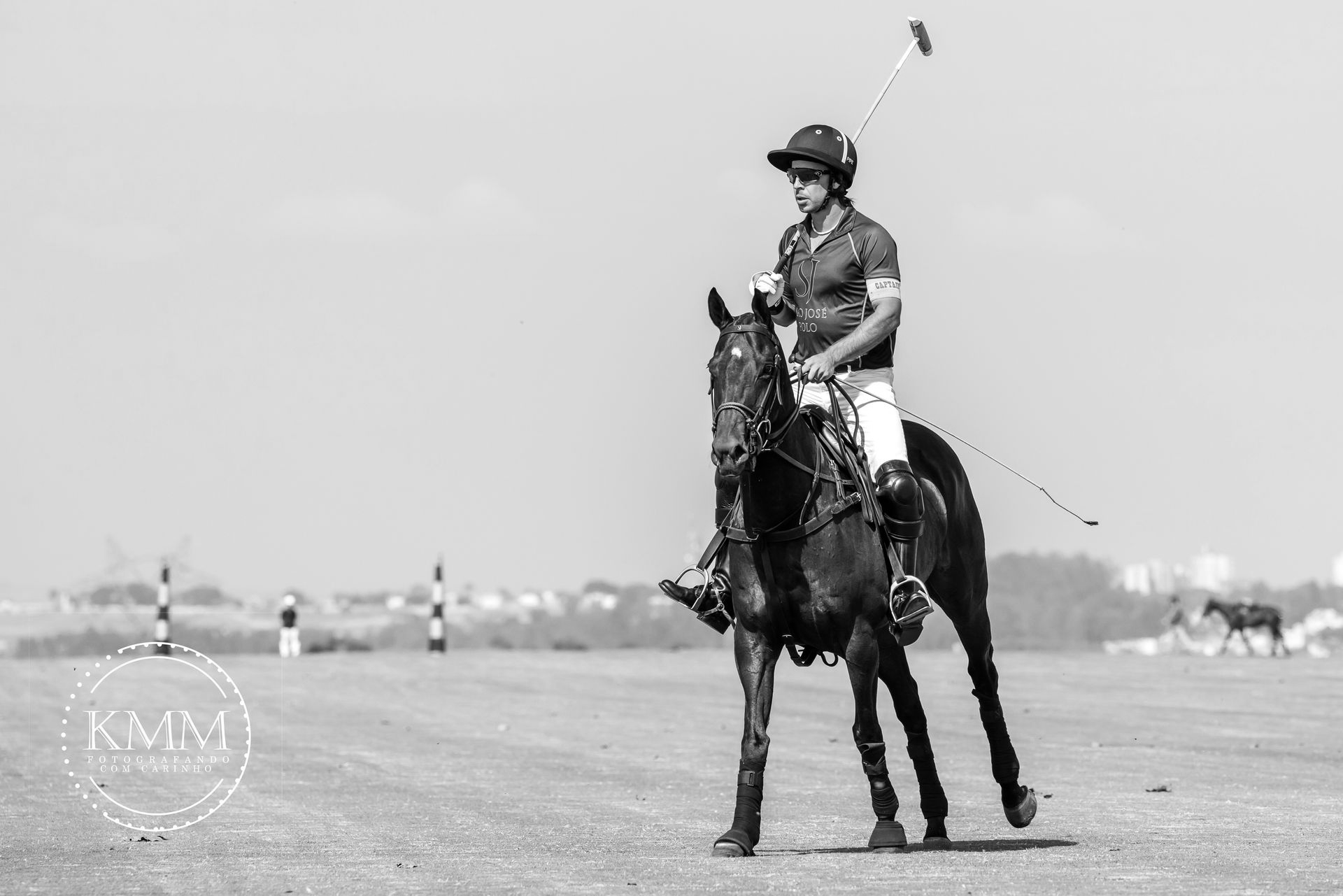 Polo player on a dark horse with mallet raised, on a field. Black and white photo.