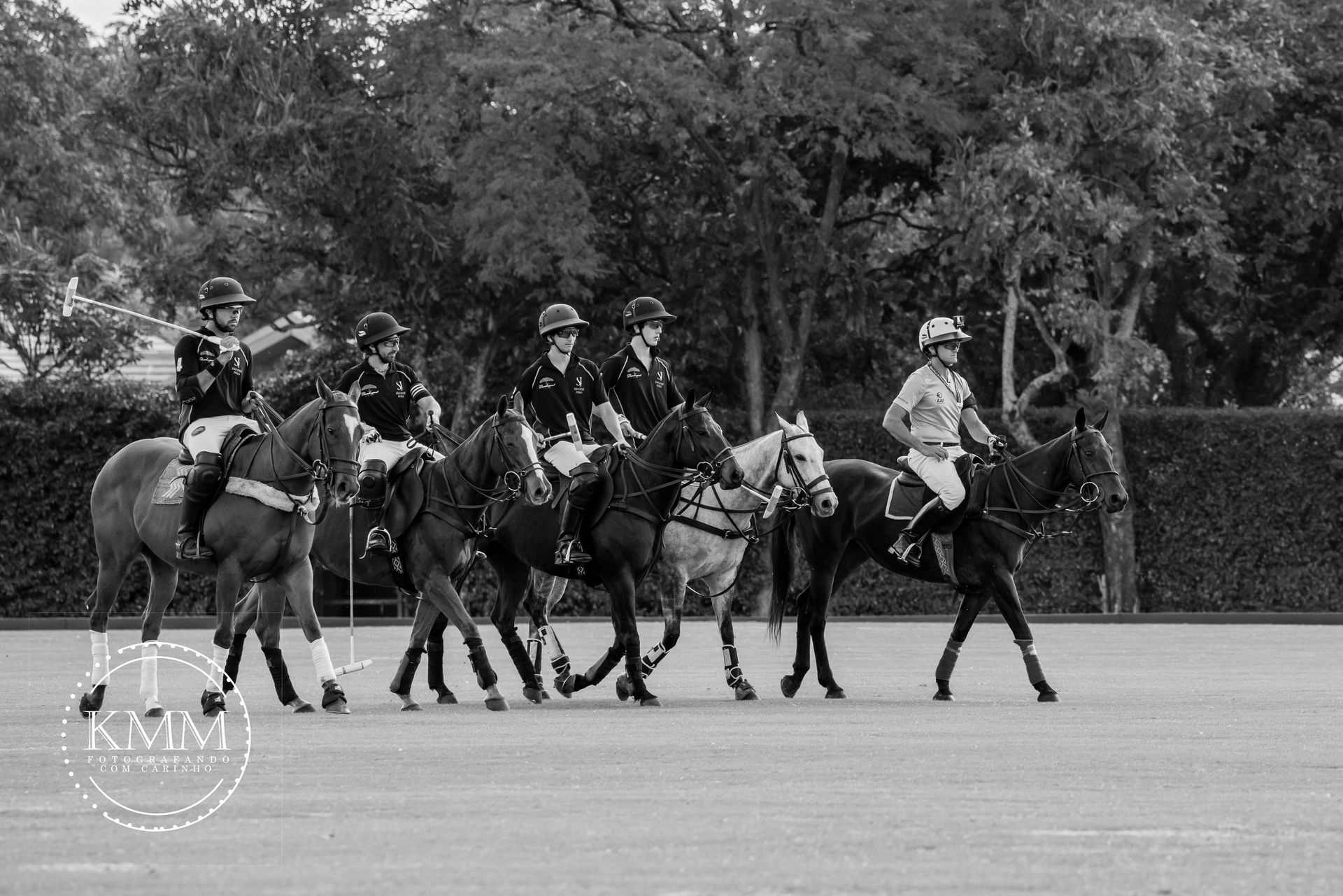 Polo players on horseback lined up on a field, in black and white.