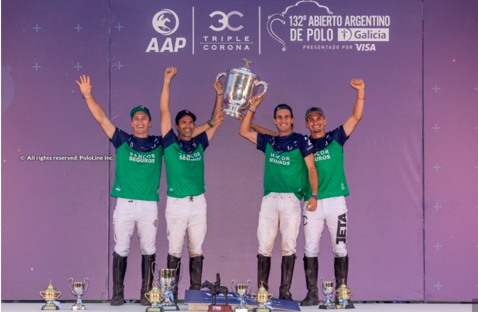 Polo team in green shirts and white pants raise trophy, celebrating victory at a tournament in front of a purple backdrop.