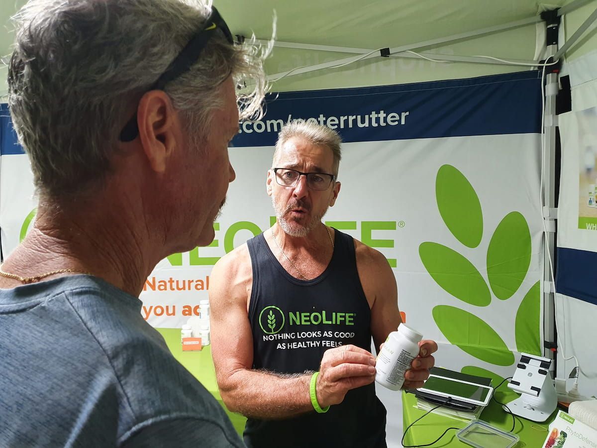 A Man Wearing A Tank Top That Says Neolife Is Talking To Another Man — Vibrant Health - Vibrant Life In Yorkeys Knob, QLD