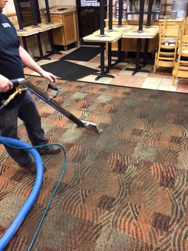 A man is cleaning a carpet in a restaurant with a vacuum cleaner.