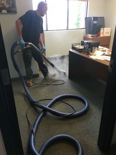 A man is using a vacuum cleaner to clean a carpet in an office.