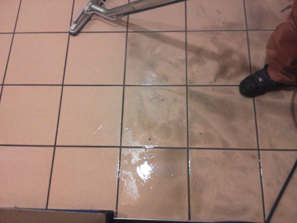 A person cleaning a tiled floor with a vacuum cleaner