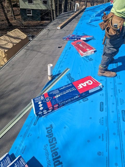 A man is standing on top of a roof covered in topshield