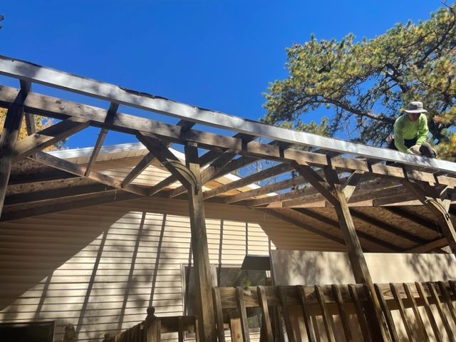 A man is standing on top of a wooden structure in front of a house.