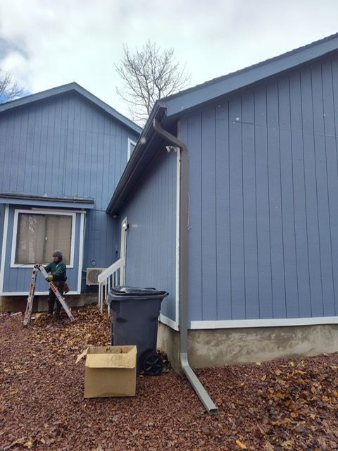 A man is sitting on a ladder in front of a blue house.