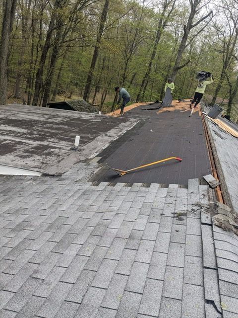 A group of people are working on a roof in the woods.