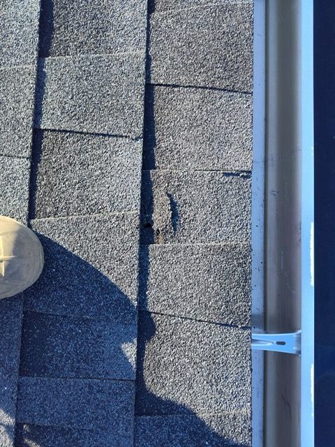 A person is standing on a roof next to a gutter.