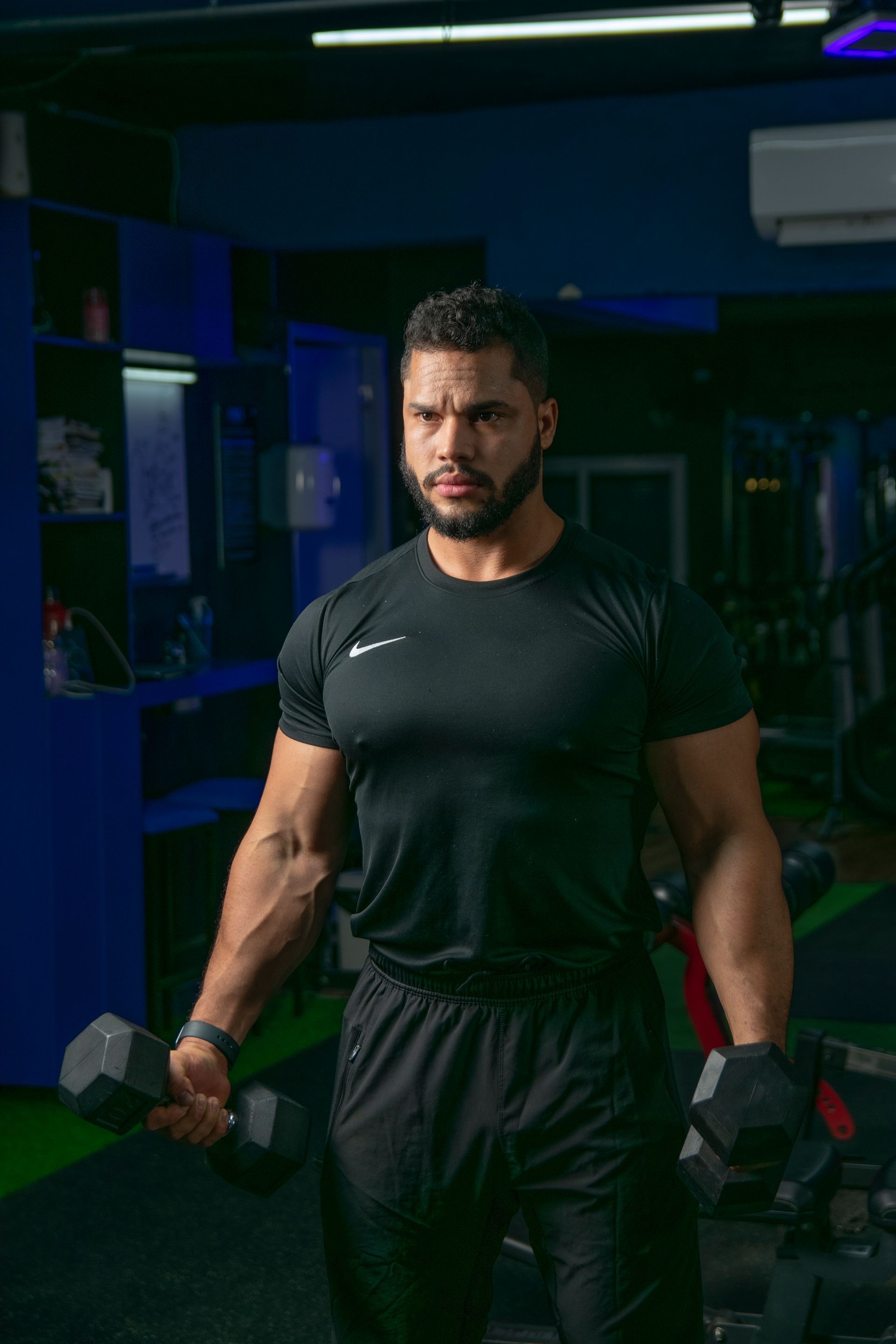 A man in a black tank top is lifting a pair of dumbbells.