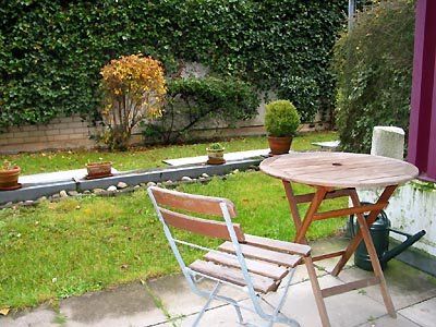 Terrasse mit Holztisch und -stuhl, grünem Rasen und mit Efeu bewachsener Mauer.