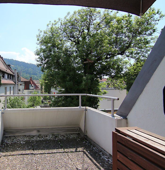 Balkon mit Blick auf die Stadt und einen großen Baum an einem sonnigen Tag.