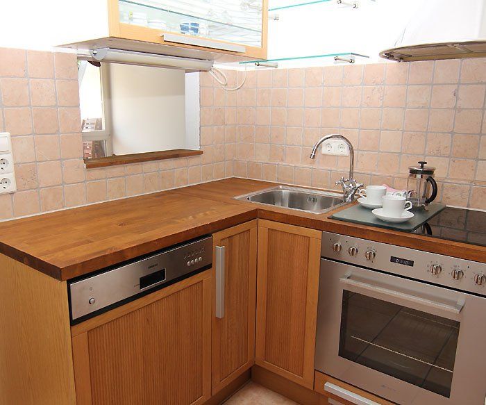 Eine Küchenecke mit Holzarbeitsplatten, Spüle, Geschirrspüler, Backofen und hellen Schränken.