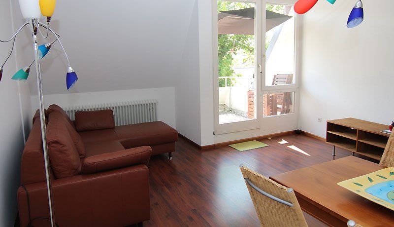 Ein braunes Ledersofa, ein Esstisch und eine Stehlampe in einem hellen Wohnzimmer mit Balkon.