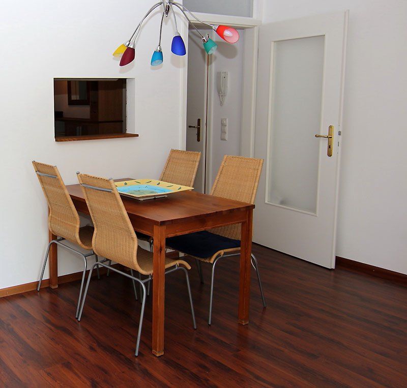 Essbereich mit Holztisch, vier Stühlen, Tür und bunter Leuchte.