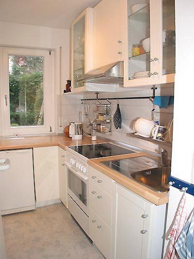 Kleine, weiße Küche mit Holzarbeitsplatten, Geräten und einem Fenster mit Blick ins Grüne.