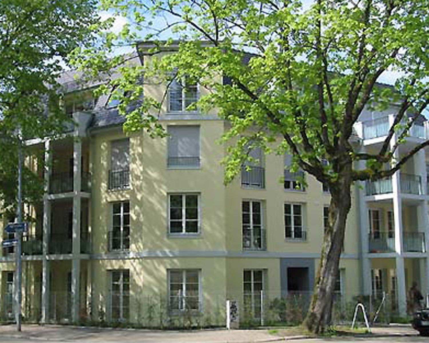 Gelbes Mehrfamilienhaus mit Balkonen, umgeben von Bäumen.