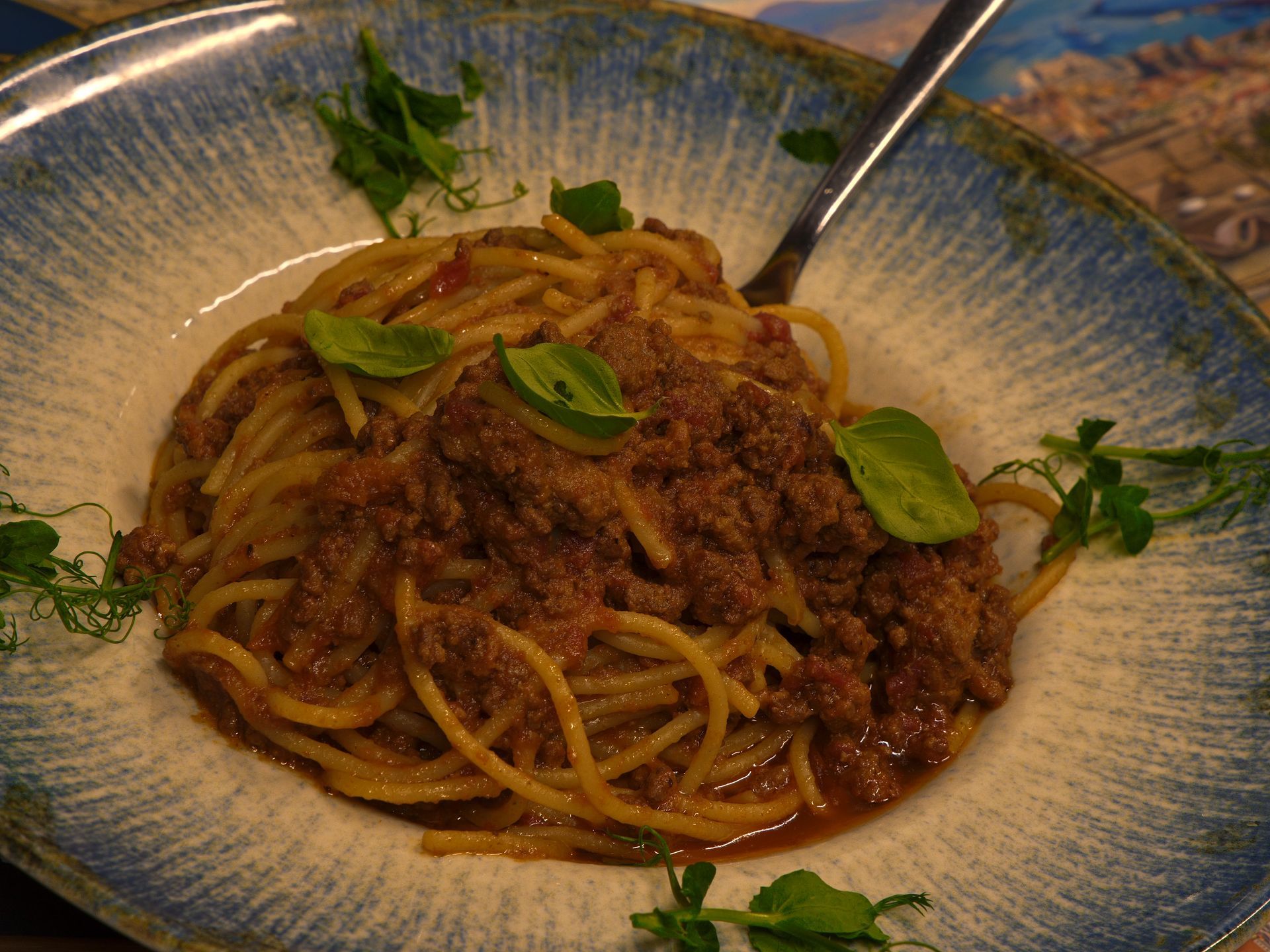 Spaghetti mit Fleischsoße, garniert mit Kräutern, in einer blau umrandeten Schüssel, mit einer Gabel.
