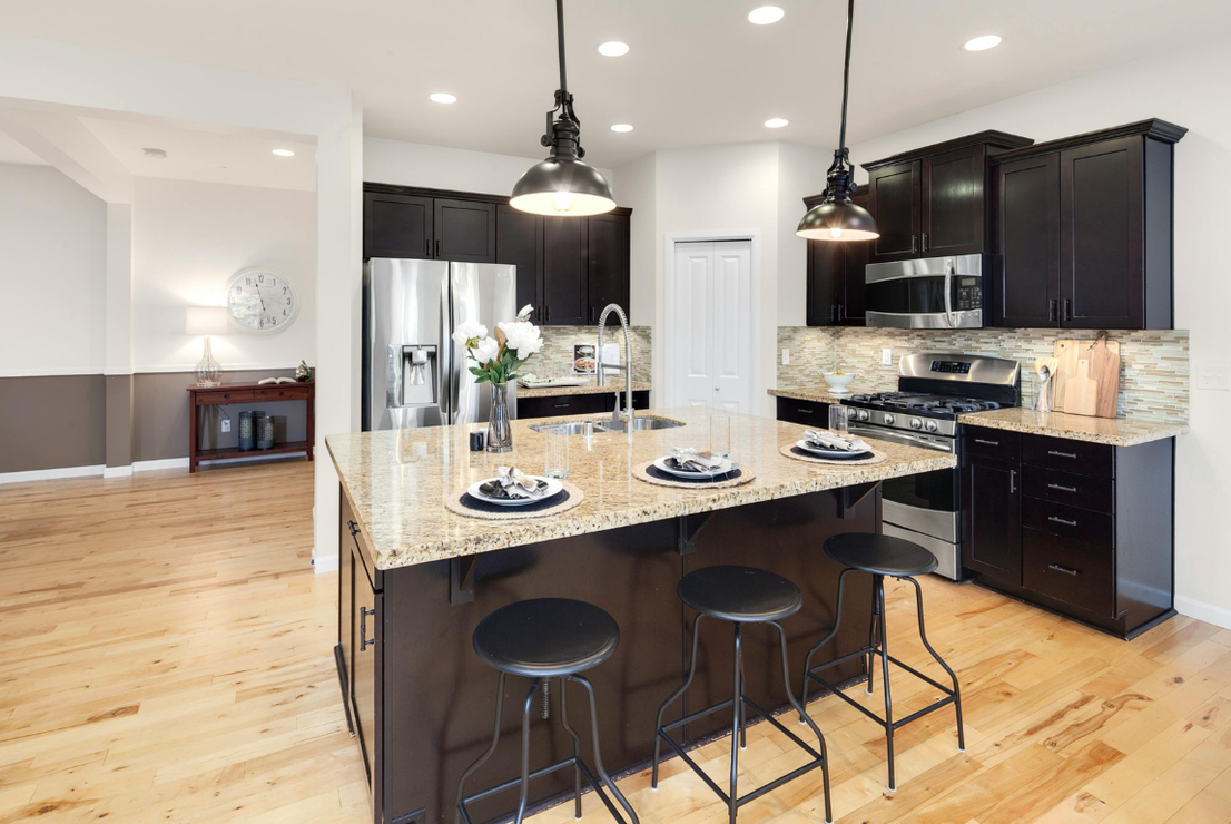 Modern kitchen with black cabinets, granite countertops, island with stools, and pendant lights.