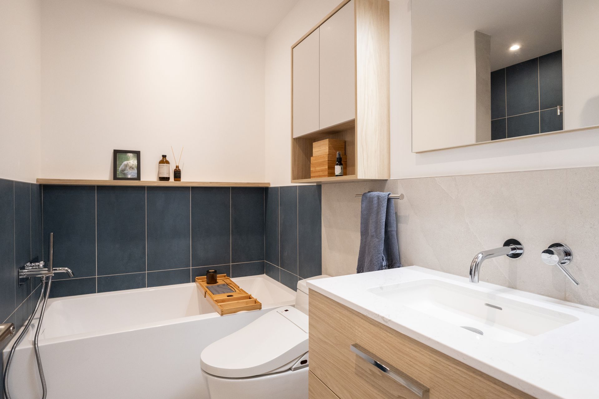 Salle de bain avec baignoire blanche, mur carrelé bleu, vanité en bois et armoire.