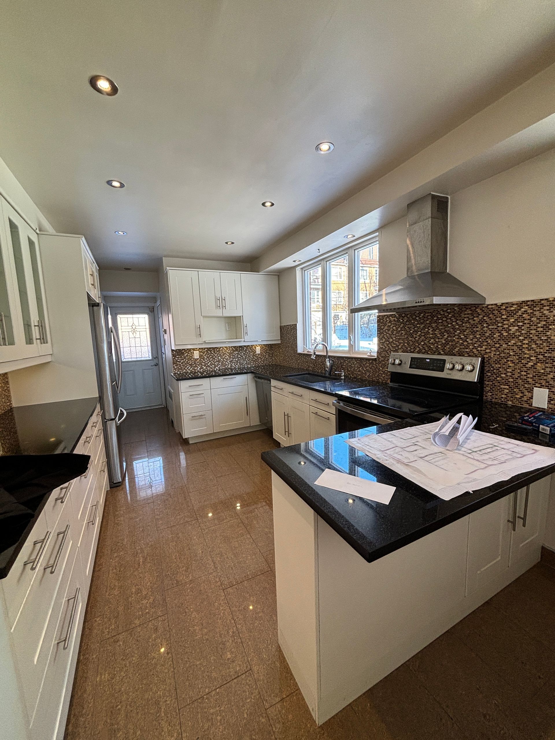 Cuisine avec armoires blanches, comptoirs foncés, dosseret brun, hotte en acier inoxydable et plancher brun moucheté.