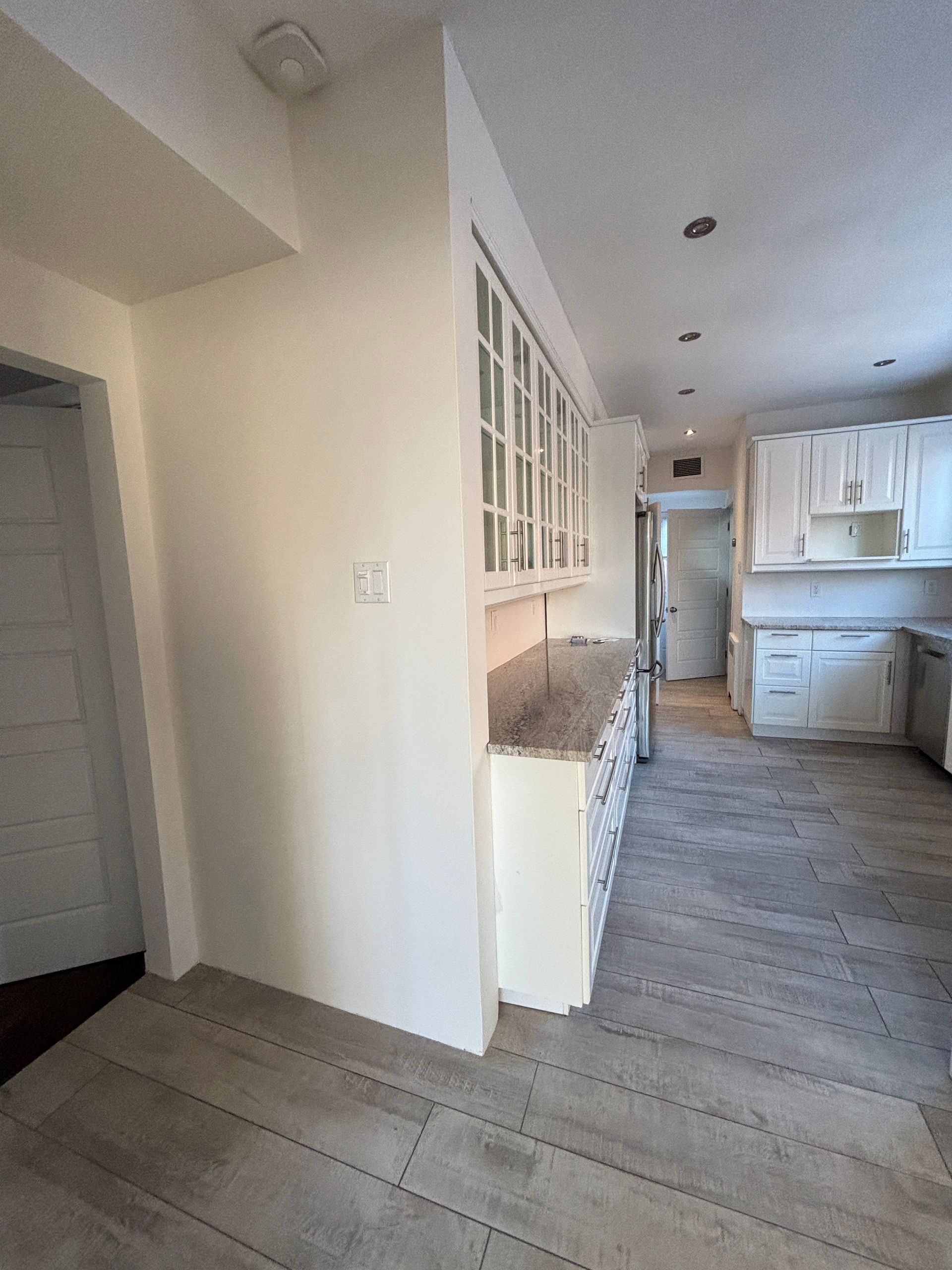 Cuisine avec armoires blanches, comptoirs gris et plancher imitation bois.